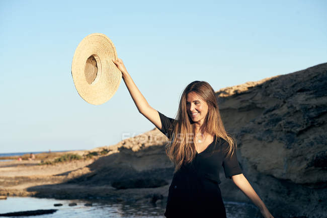 Jovem mulher sorridente olhando para longe na costa rochosa — Fotografia de Stock