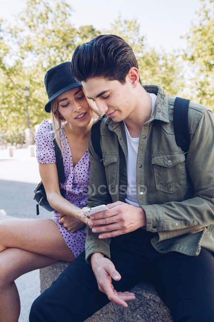 Joven hombre guapo con novia usando el teléfono mientras está sentado en un hermoso jardín - foto de stock