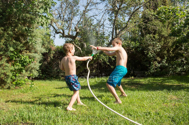 Маленькие дети в купальниках бегают и брызгают водой из садового шланга друг на друга — стоковое фото