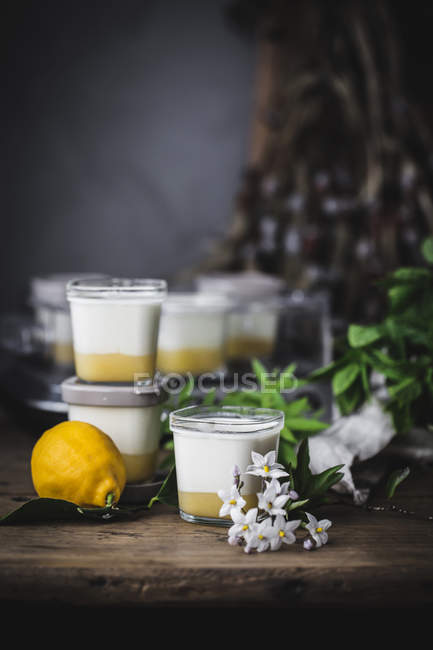 Gestapelte Gläser mit hausgemachtem Joghurt und Zitronenquark auf mit Blumen dekorierter Holzoberfläche — Stockfoto