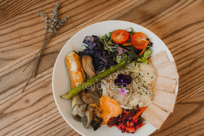 Сверху тарелка со спелыми сочными помидорами, овощами салата, хрустящим хлебом на деревянном столе — стоковое фото