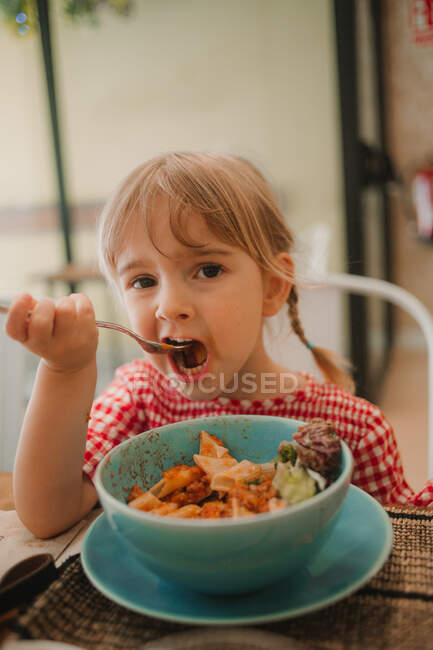 Appetizing fragrant assorted food in blue bowl and adorable girl eating at table — Stock Photo