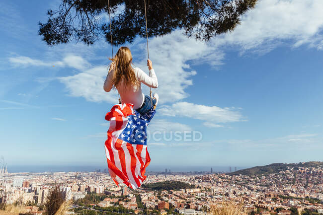 Jeune fille célébrant le 4 juillet avec le drapeau américain sur une balançoire — Photo de stock
