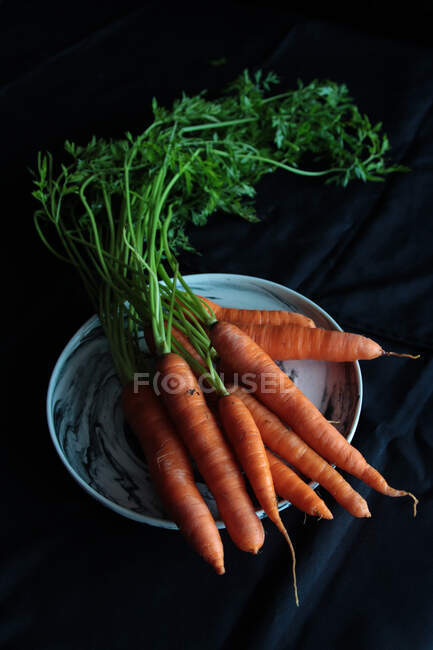 Ripe orange carrots with tops on plate — Stock Photo