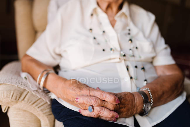 Imagem cortada de mulher sênior em camisa branca e com contas no pescoço sentado em casa — Fotografia de Stock