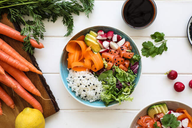 Du dessus bol de riz bouilli délicieux avec divers légumes frais placés sur une table blanche près de la sauce soja — Photo de stock