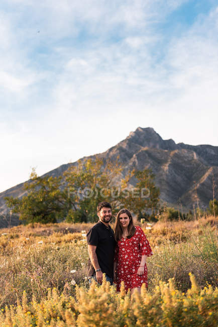 Homem e sorrindo grávida esposa olhando para a câmera no fundo da natureza e da montanha — Fotografia de Stock