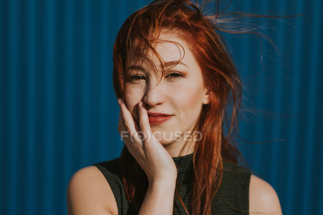 Lächelnde Frau, die im Sonnenlicht schielt und das Wetter vor blauer Wand genießt — Stockfoto