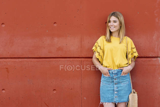Jeune femme blonde gaie debout sur fond orange et regardant loin — Photo de stock