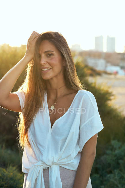 Молода усміхнена жінка в білому одязі, що стоїть на сонячному світлі — стокове фото