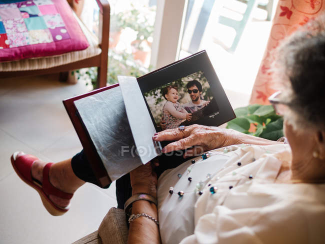 From above of senior woman in glasses looking at photo of granddaughter in album at home — Stock Photo