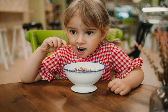 Appetizing fragrant food in white bowl and adorable girl eating with hands at table — Stock Photo