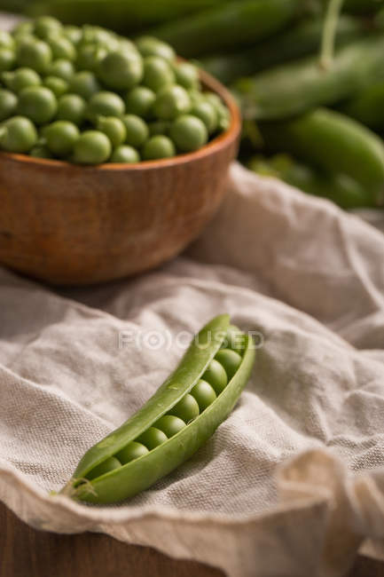 Peeled open pea pod on white cloth with bowl of peas — Stock Photo