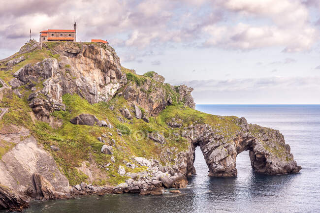 Vue pittoresque du bord de mer rocheux avec bâtiment sur fond d'eau calme et ciel nuageux — Photo de stock