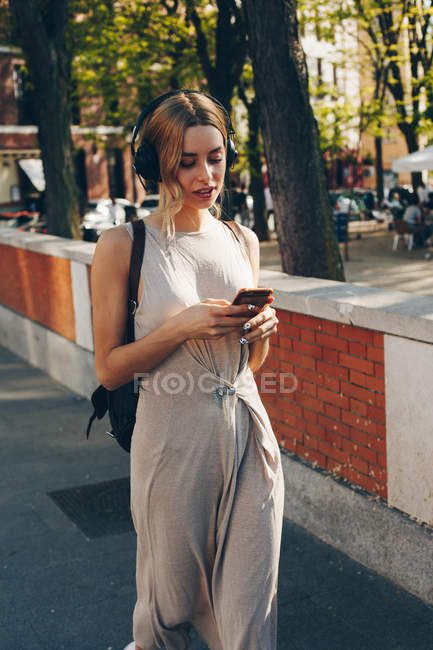Mulher atraente em vestido de verão longo ouvir música durante a caminhada na rua à luz do dia — Fotografia de Stock