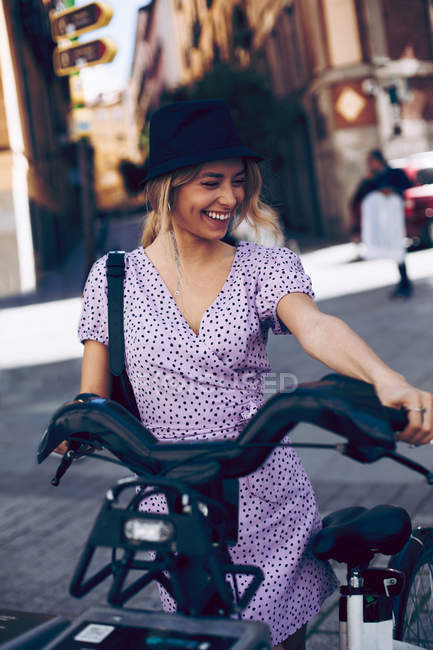 Attrayant joyeux jeune femme prenant un vélo de location dans la rue de la ville — Photo de stock