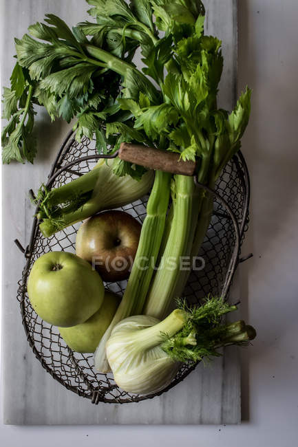 Von oben Metallkorb mit Äpfeln, Sellerie und Fenchelzwiebeln auf weißem Hintergrund — Stockfoto