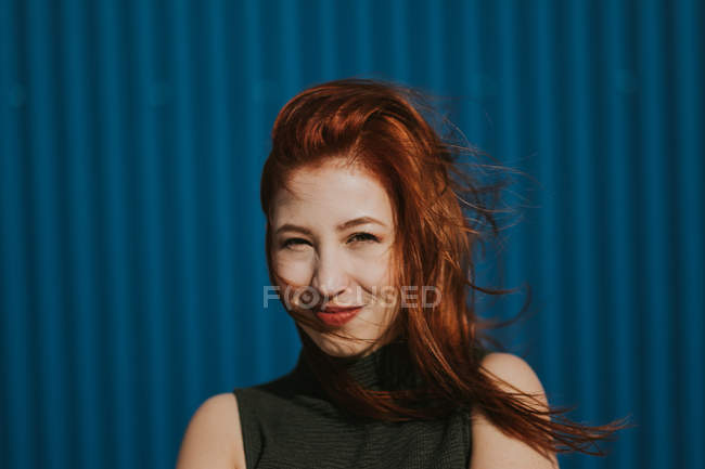 Lächelnde Frau, die im Sonnenlicht schielt und das Wetter vor blauer Wand genießt — Stockfoto