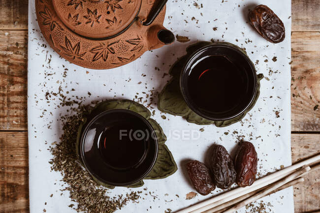 Von oben duftenden leckeren Tee in Tasse Ton Teekanne und süße Datteln auf weißem Tablett mit Teeblättern auf Holzgrund dekoriert — Stockfoto