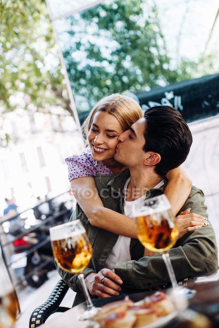 Весела молода приваблива пара цілується, насолоджуючись освіжаючими напоями — стокове фото