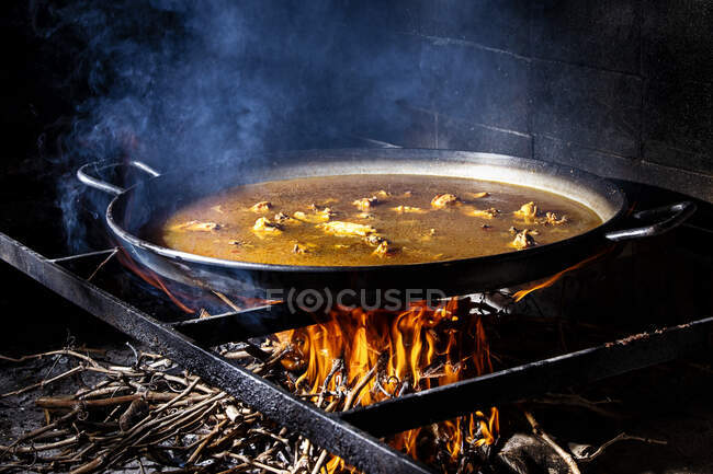Große eiserne Pfanne mit kochender Brühe zum Kochen von Paella über offenem Feuer mit Holz — Stockfoto