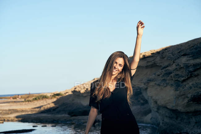 Молода усміхнена жінка дивиться на кам'янисте узбережжя — стокове фото