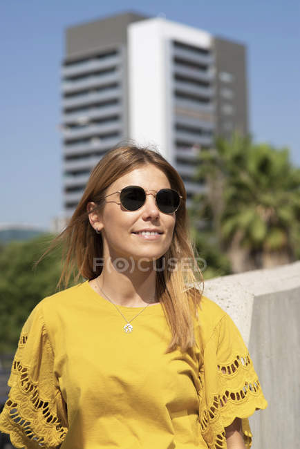 Fröhliche junge Frau mit Sonnenbrille lächelt und schaut in der Stadt weg — Stockfoto