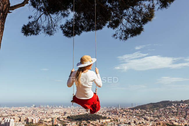 Fille s'amuser avec jupe rouge et chapeau balançant tout en contemplant la ville en arrière-plan — Photo de stock