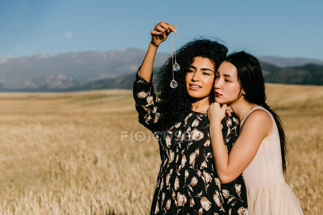 Woman leaning on shoulder of friend while standing in field holding glass pieces — Stock Photo