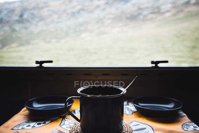 Tasse en métal avec de la nourriture chaude et des bols vides placés sur la table près de la fenêtre d'une maison de campagne — Photo de stock
