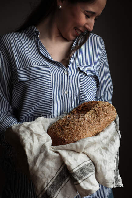 Femme souriante tenant savoureux pain appétissant sur une serviette en tissu dans les mains sur fond noir — Photo de stock