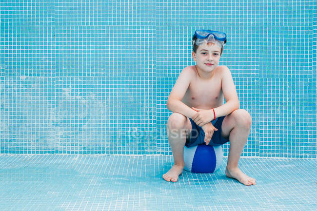 Menino sentado na bola na piscina vazia — Fotografia de Stock