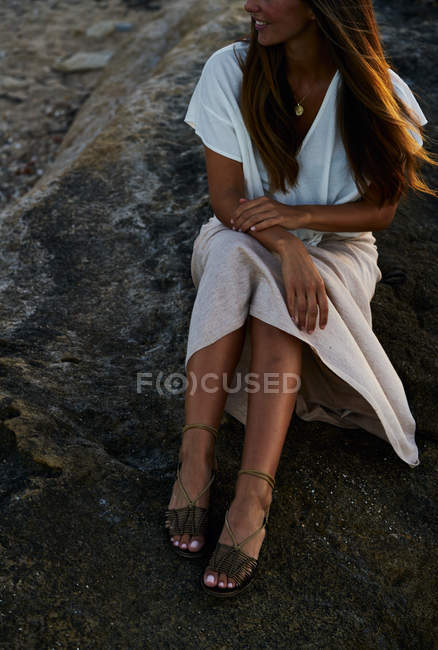 Joven modelo femenino sentado en la roca y mirando hacia otro lado - foto de stock