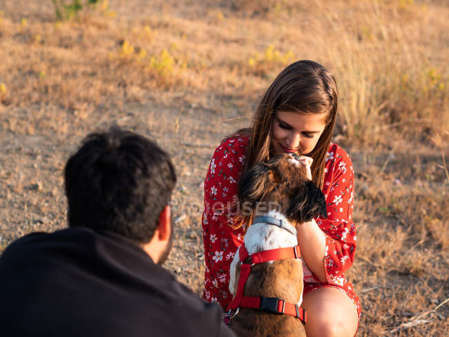 Усміхнена пара сидить серед високої трави і розважається з маленькою собакою в сільській місцевості — стокове фото