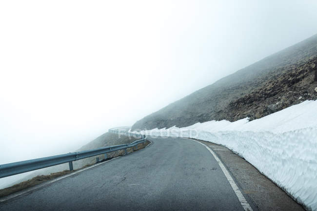 Асфальтована дорога через засніжену гірську місцевість в туманний день — стокове фото