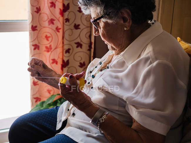 Вид сбоку пожилой женщины в рубашке и очках, сидящей дома на кресле — стоковое фото