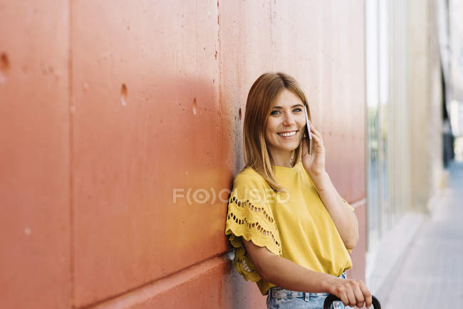 Young woman talking on mobile phone leaning on red wall — Stock Photo