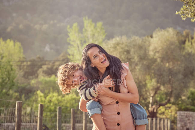Lachende Mutter und Sohn haben Spaß beim Huckepack auf dem Land — Stockfoto