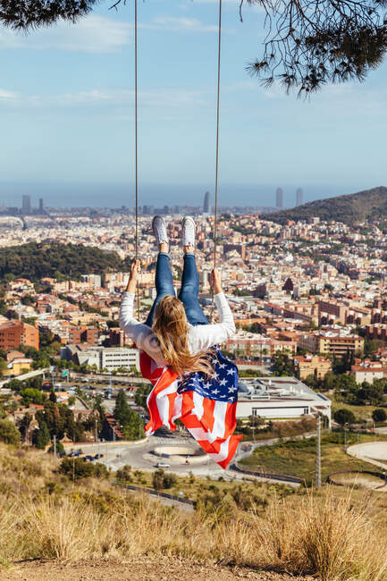 Юная девушка празднует 4 июля с американским флагом на качелях — стоковое фото