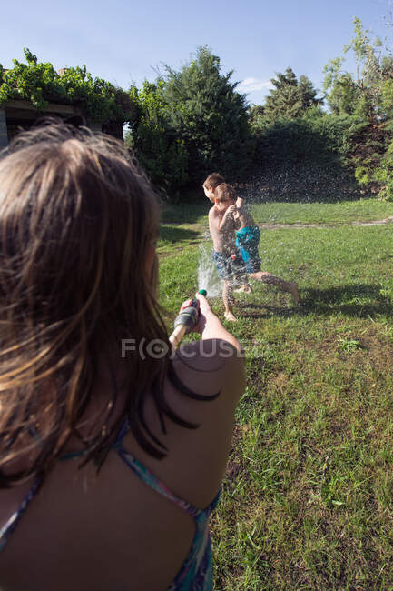 Kleine Kinder in Badebekleidung rennen herum und spritzen sich gegenseitig Wasser aus dem Gartenschlauch zu, Ich-Perspektive — Stockfoto