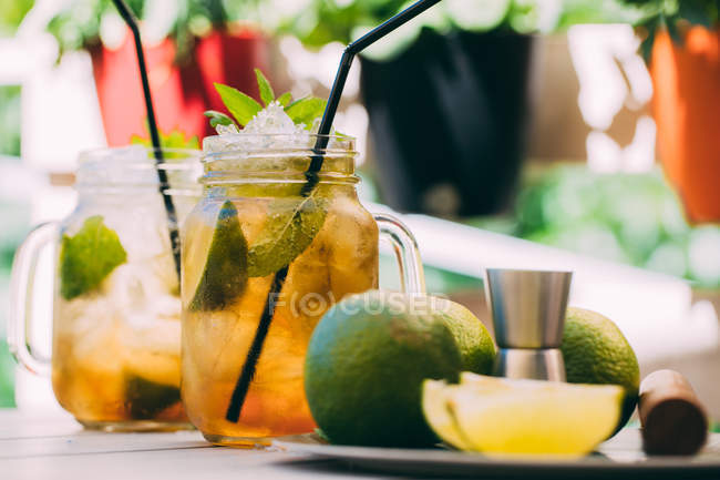 Deux cocktails mojito préparés avec du citron vert, de la menthe, du rhum, de la soude et de la glace dans des bocaux en maçon sur la table à l'extérieur — Photo de stock