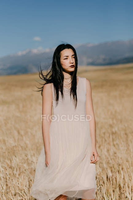 Mulher asiática bonita olhando para longe, enquanto de pé no fundo borrado do prado no dia ventoso na natureza — Fotografia de Stock