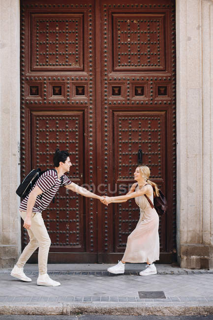Jeune couple joyeux et ludique en vêtements décontractés s'amuser pendant sortir ensemble en plein air devant la belle vieille porte — Photo de stock