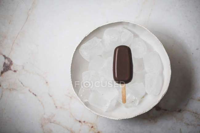 Chocolate ice cream popsicle on plate with ice cubes on a marble surface — Stock Photo