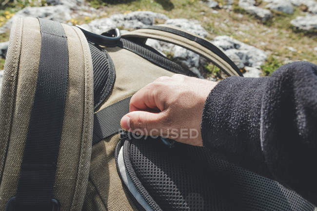 Обрізати чоловіка рукою в теплий светр, застібаючи мандрівний рюкзак під час подорожі в сонячну погоду — стокове фото