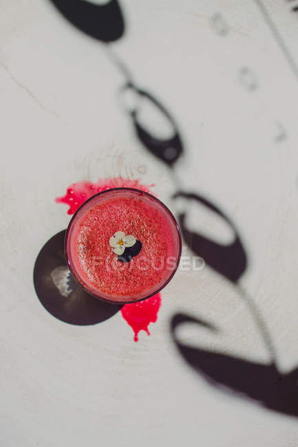 Bolla schiumosa gustoso profumato frullato rosa decorato con fiore in vetro su superficie bianca con ombra — Foto stock