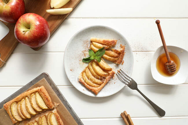 Зверху шматок смачного яблучного пирога з медом і листям м'яти з корицею, розміщеною на тарілці на білому столі — стокове фото