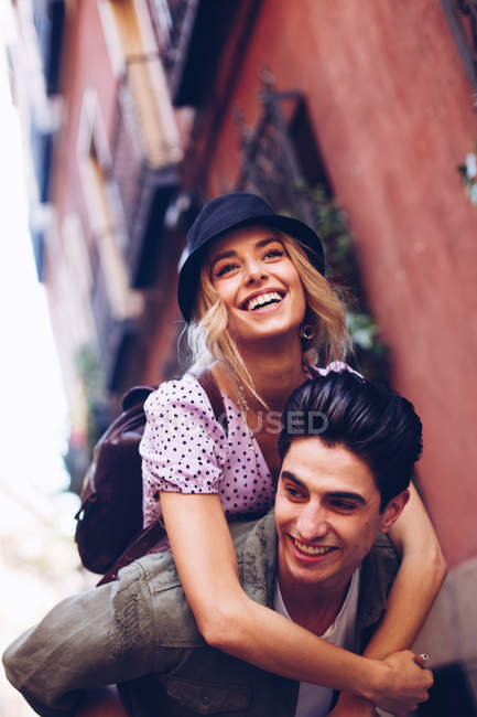 Молодой веселый мужчина катает женщину на спине во время свиданий на открытом воздухе — стоковое фото