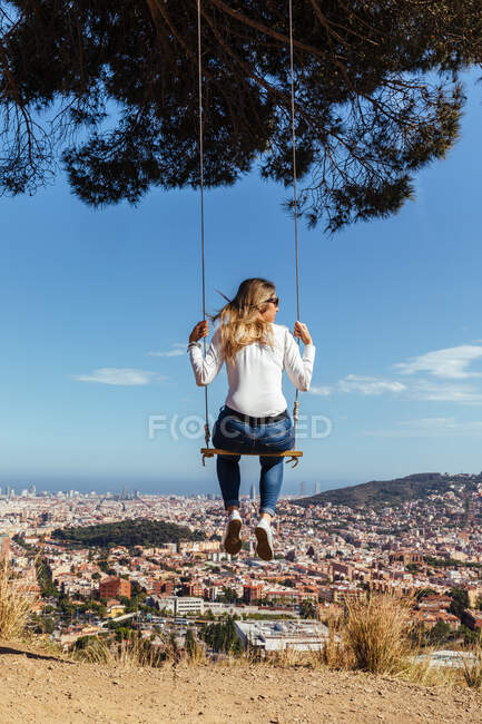 Blonde fille balançant avec vue sur la ville en arrière-plan — Photo de stock