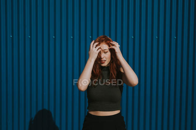 Усміхнена жінка, що кліпає на сонці і насолоджується погодою з синьою стіною. — стокове фото